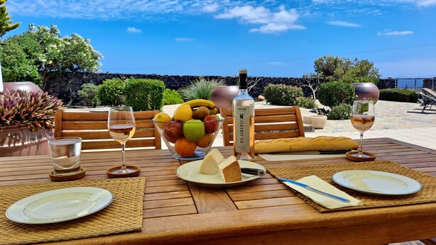A table set for a meal with a view of the ocean, a stone wall, and various fruits and beverages. - Villa Essence - with A/C, heated private pool, hottub, gardens & stunning views! (Tias)