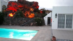 A swimming pool with a rocky backdrop and a white building with a door and windows. - Villa Essence - with A/C, heated private pool, hottub, gardens & stunning views! (Tias)
