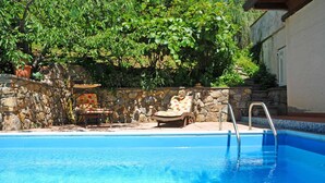 A swimming pool with a stone wall and a lounge chair.