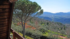 A wooden cabin with a balcony overlooking a mountainous landscape with trees and a clear sky.