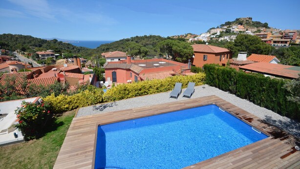A swimming pool with wooden deck, surrounded by greenery and houses with red roofs.