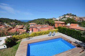 A swimming pool with wooden deck, surrounded by greenery and houses with red roofs. - Holiday rental villa with swimming pool in Begur, Begur (Begur)