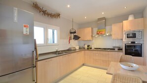 A modern kitchen with stainless steel appliances, wooden cabinets, and a dining area with wicker chairs.