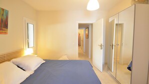 A bedroom with a bed, a wardrobe, and a hallway leading to another room.