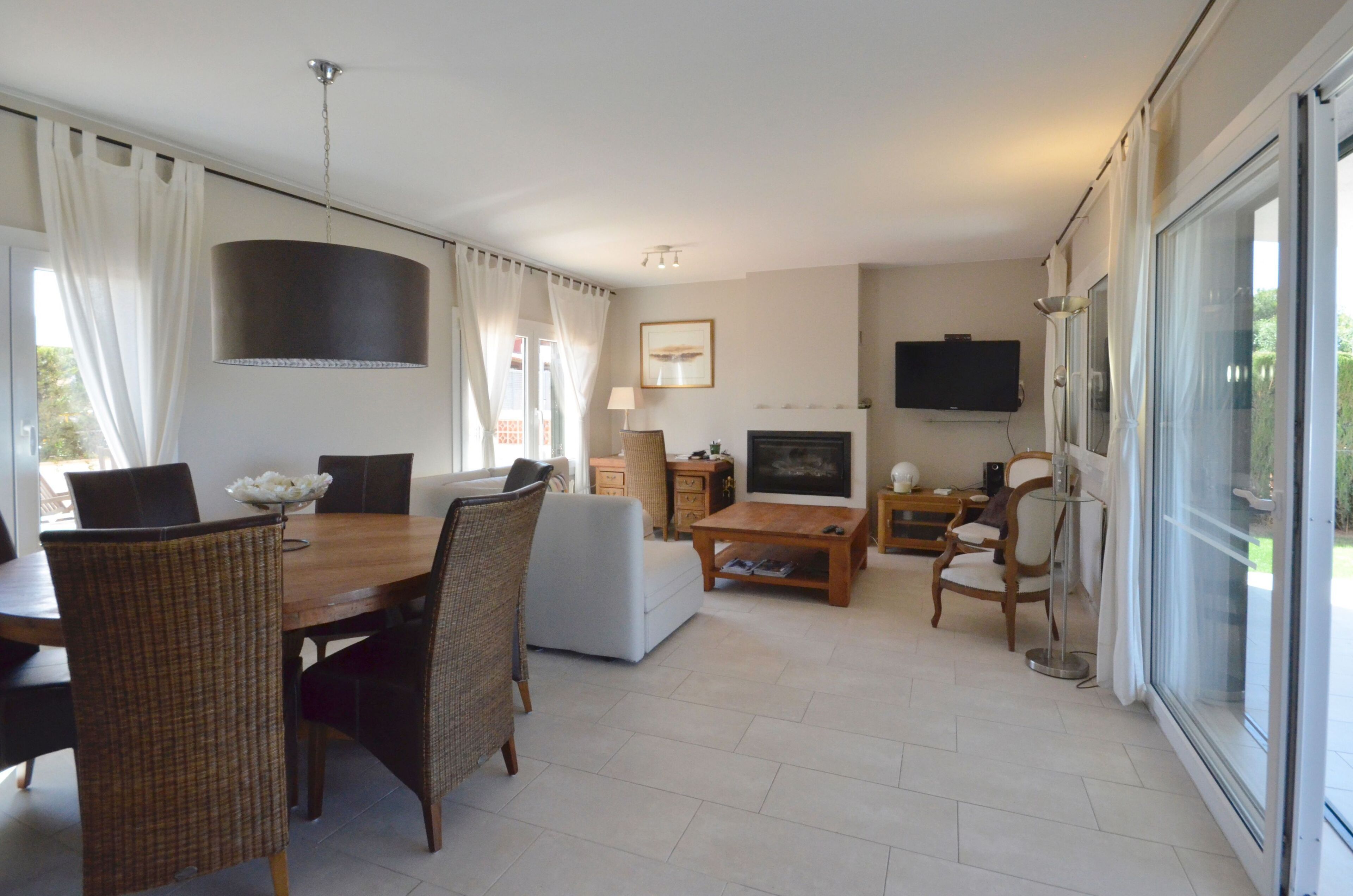 A spacious living room with a dining area, a fireplace, and a television mounted on the wall.