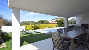 A covered outdoor patio with a pool, lounge chairs, and a dining table.