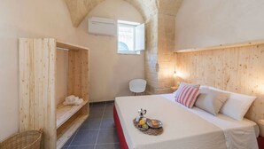 Una habitación acogedora con techo abovedado de piedra, una cama de madera con almohadas, una mesita con una bandeja de comida y una silla blanca.