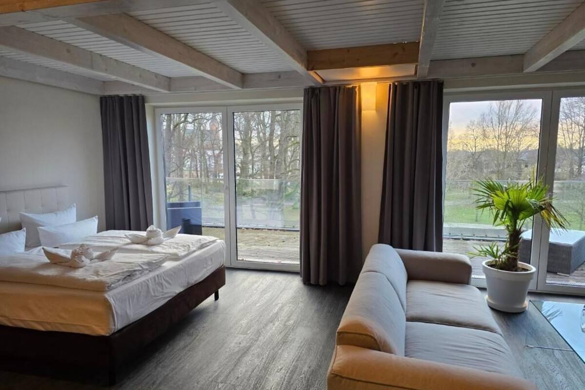 A modern hotel room with a large bed, a sofa, and a potted plant.