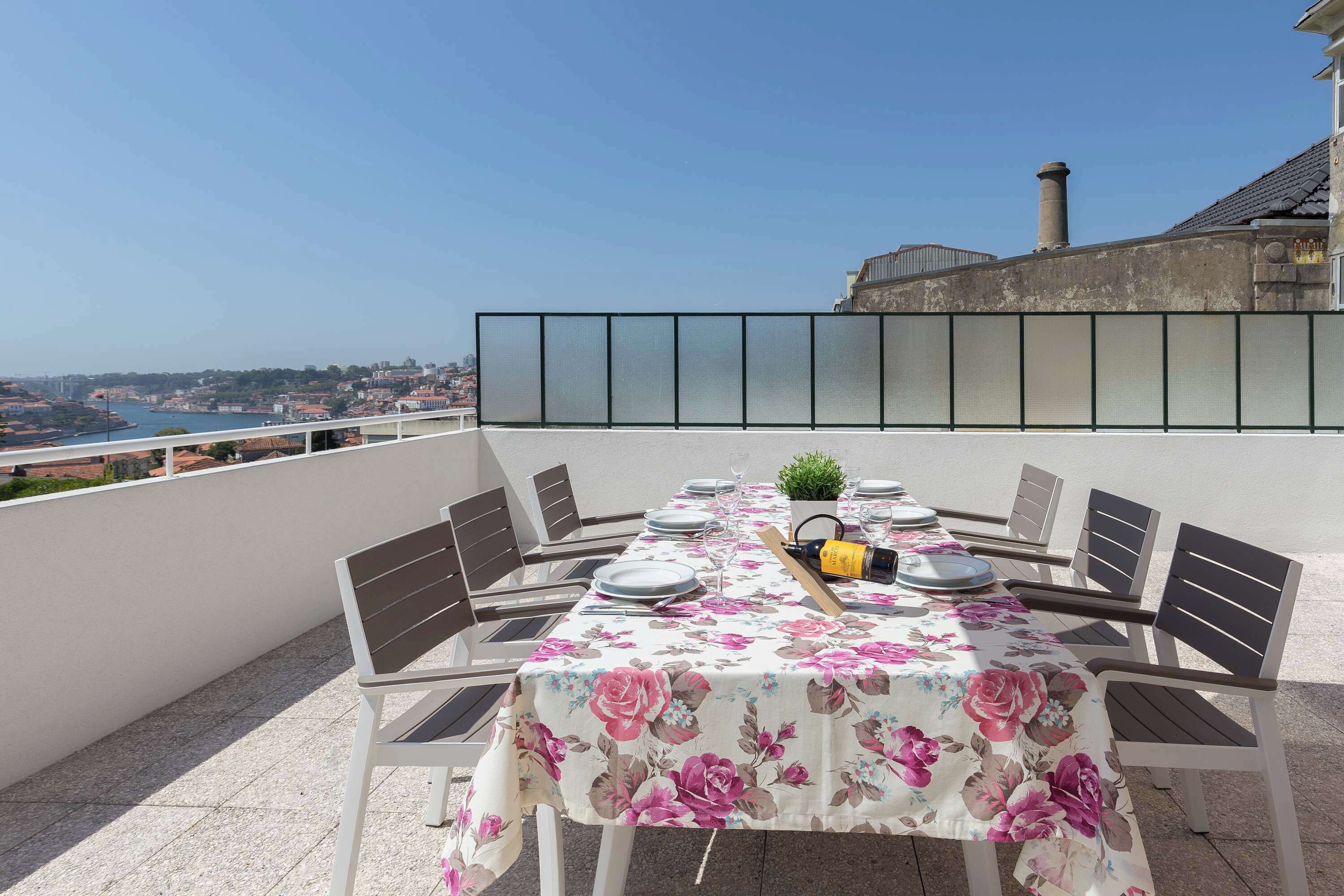 Una mesa de comedor con sillas, una botella y una planta en maceta en una terraza con vista a la ciudad.
