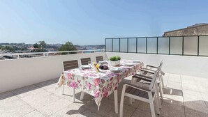 A rooftop terrace with a table set for dining, chairs, a potted plant, and a view of the city. - Anna´s Flats by HostWise (Vila Nova de Gaia)