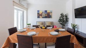 A dining area with a table set for four, a sofa, a TV, and a plant. - Anna´s Flats by HostWise (Vila Nova de Gaia)