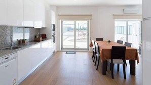 A modern kitchen with white cabinets, a granite countertop, and a dining area with a table and chairs. - Anna´s Flats by HostWise (Vila Nova de Gaia)