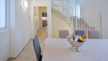 Un comedor moderno con una mesa dispuesta para dos personas, un cuenco plateado con una botella de champán y una escalera que conduce a un nivel superior.