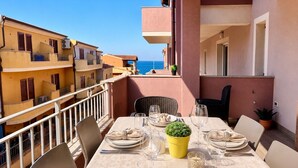 A dining table set for four on a balcony with a view of the sea, surrounded by buildings. - New Construction,  beautiful 2 bed apartment facing the sea, Wi-fi ,Aircon (La Ciaccia)