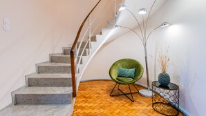 A modern staircase with a wooden handrail, a green chair with a blue cushion, and a floor lamp with three lights. - UNIQUE DUPLEX PENTHOUSE & FREE PARKING (Porto)
