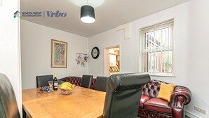 A dining area with a wooden table, leather chairs, and a red leather sofa. - Spacious 3 Bedroom House in Wigan – Perfect for Contractors & Families (Hindley)