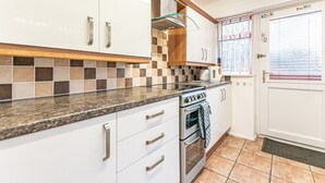 A kitchen with white cabinets, a granite countertop, a stainless steel oven, and a window with blinds. - Spacious 3 Bedroom House in Wigan – Perfect for Contractors & Families (Hindley)