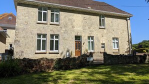 Un bâtiment en pierre de deux étages, avec un toit en tuiles, une entrée centrale dotée d’une porte en bois et un mur en pierre à l’avant.