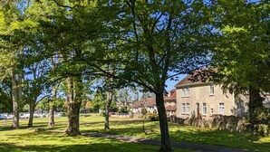 Un parc avec un sentier pédestre, des arbres et un bâtiment en pierre surmonté d’un toit rouge.