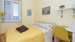 A bedroom with a bed, a desk, a chair, a window, and a shelf with plants. - Vera Seaview Apartment (Zadar)