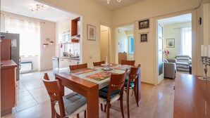 A dining area with a wooden table and chairs, a chandelier, and a kitchen in the background. - Vera Seaview Apartment (Zadar)