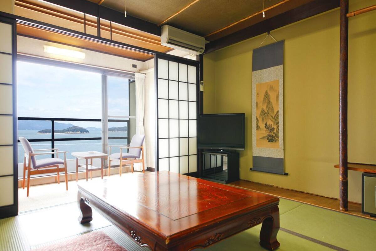 Ein traditioneller japanischer Raum mit Tatami-Böden, einem niedrigen Holztisch, einem Fernseher und Meerblick.