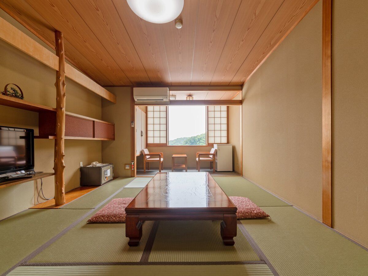 A traditional Japanese room with tatami flooring, a low table, a television, and a view of a mountain.