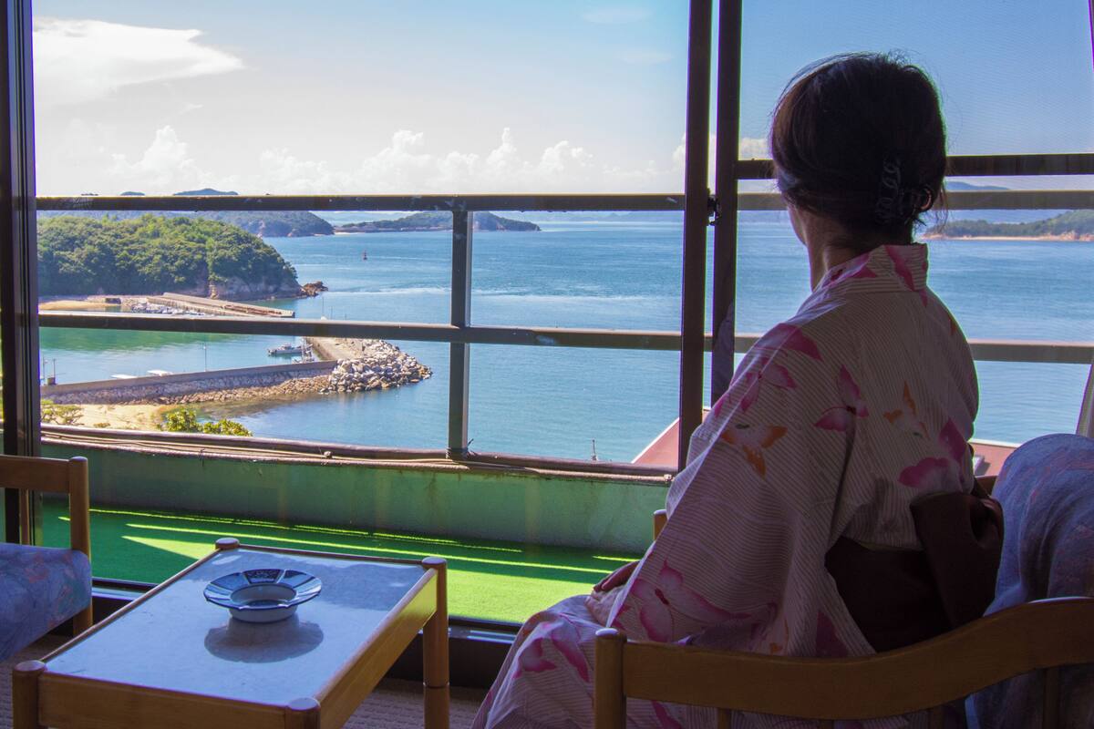 Ein Zimmer mit einem großen Fenster und Blick auf die Küste, einem Tisch mit Teller und einem Stuhl.