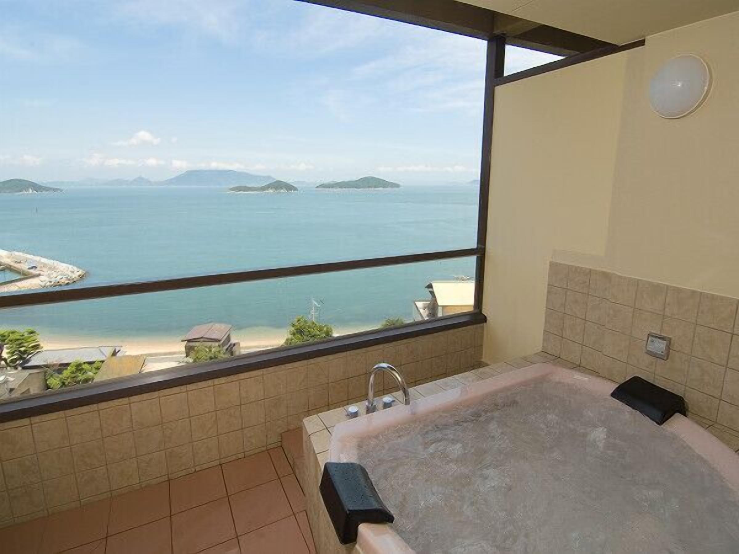 A bathroom with a bathtub, a window with a view of the sea, and tiled walls.