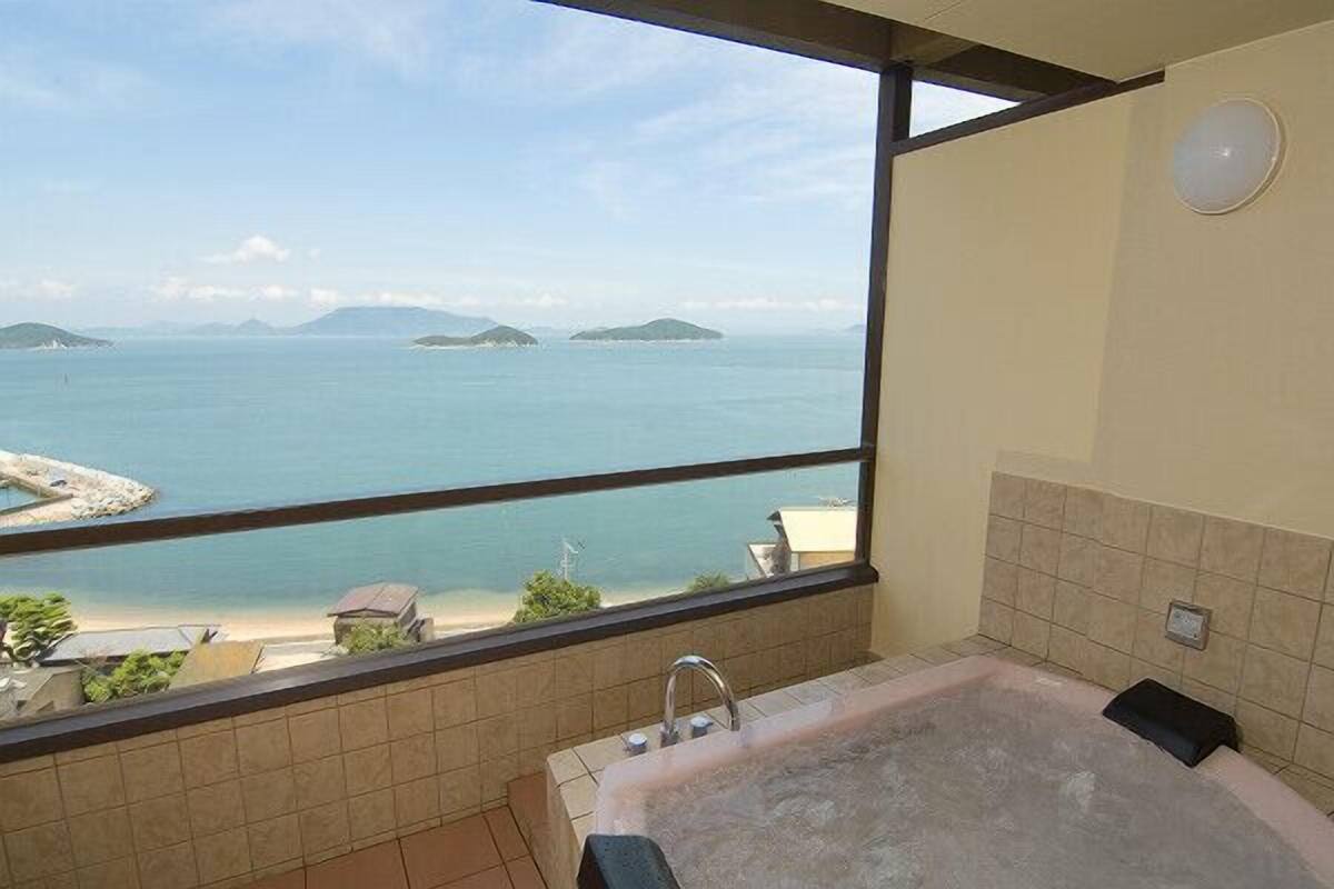 Ein Badezimmer mit einer Badewanne, einem Fenster mit Meerblick und gefliesten Wänden.