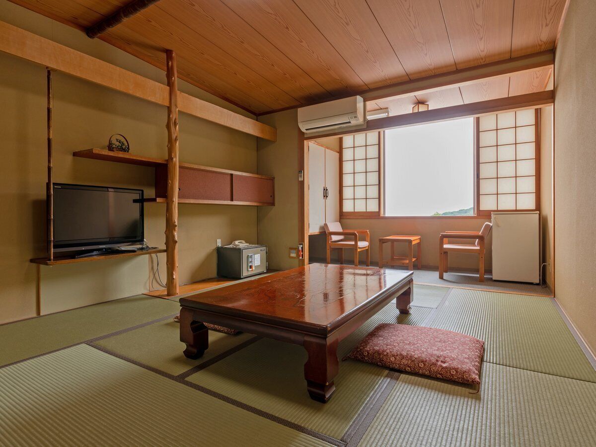 A traditional Japanese room with tatami flooring, a low wooden table, a television, and a sliding door leading to a balcony.