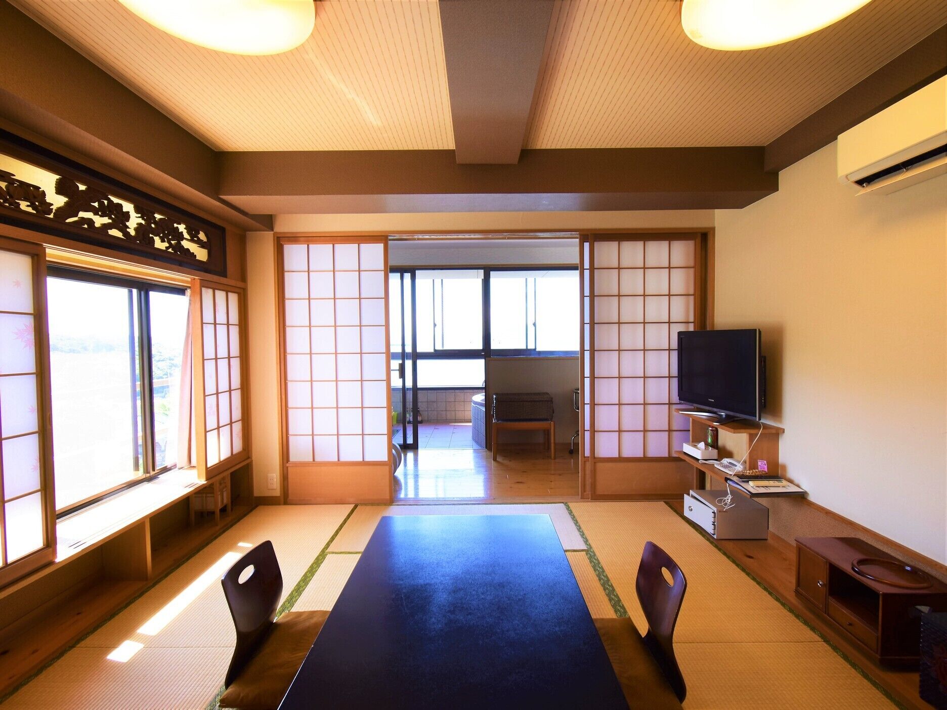 A traditional Japanese room with tatami flooring, a low table, chairs, a television, and sliding doors.