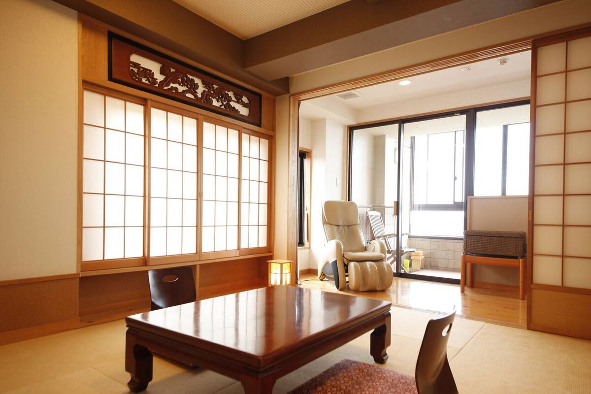 Ein traditioneller japanischer Raum mit Tatami-Bodenbelag, einem niedrigen Holztisch, einer gepolsterten Sitzbank und verschiebbaren Türen.
