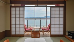 A traditional Japanese room with tatami flooring, a low wooden table, two red chairs, and a sliding shoji screen.