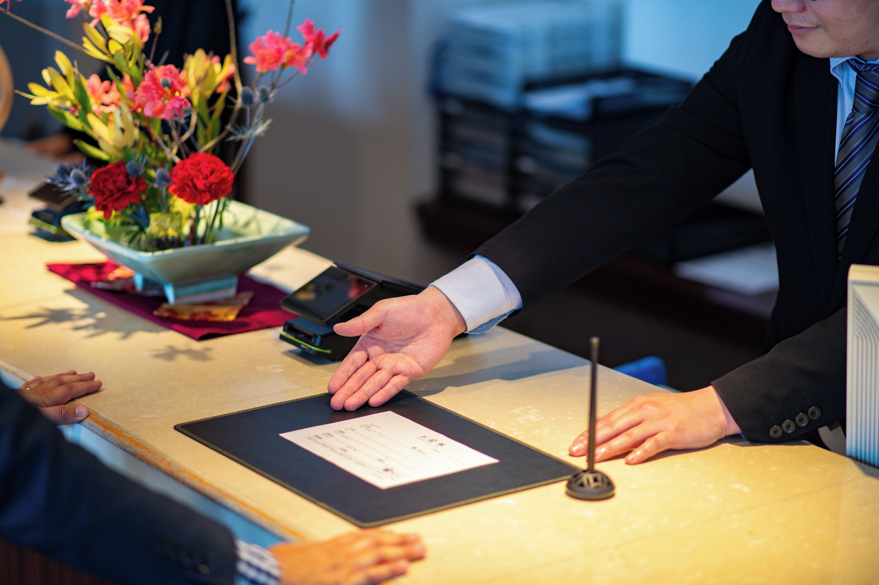 A reception desk with a vase of flowers, a tablet, and a clipboard.