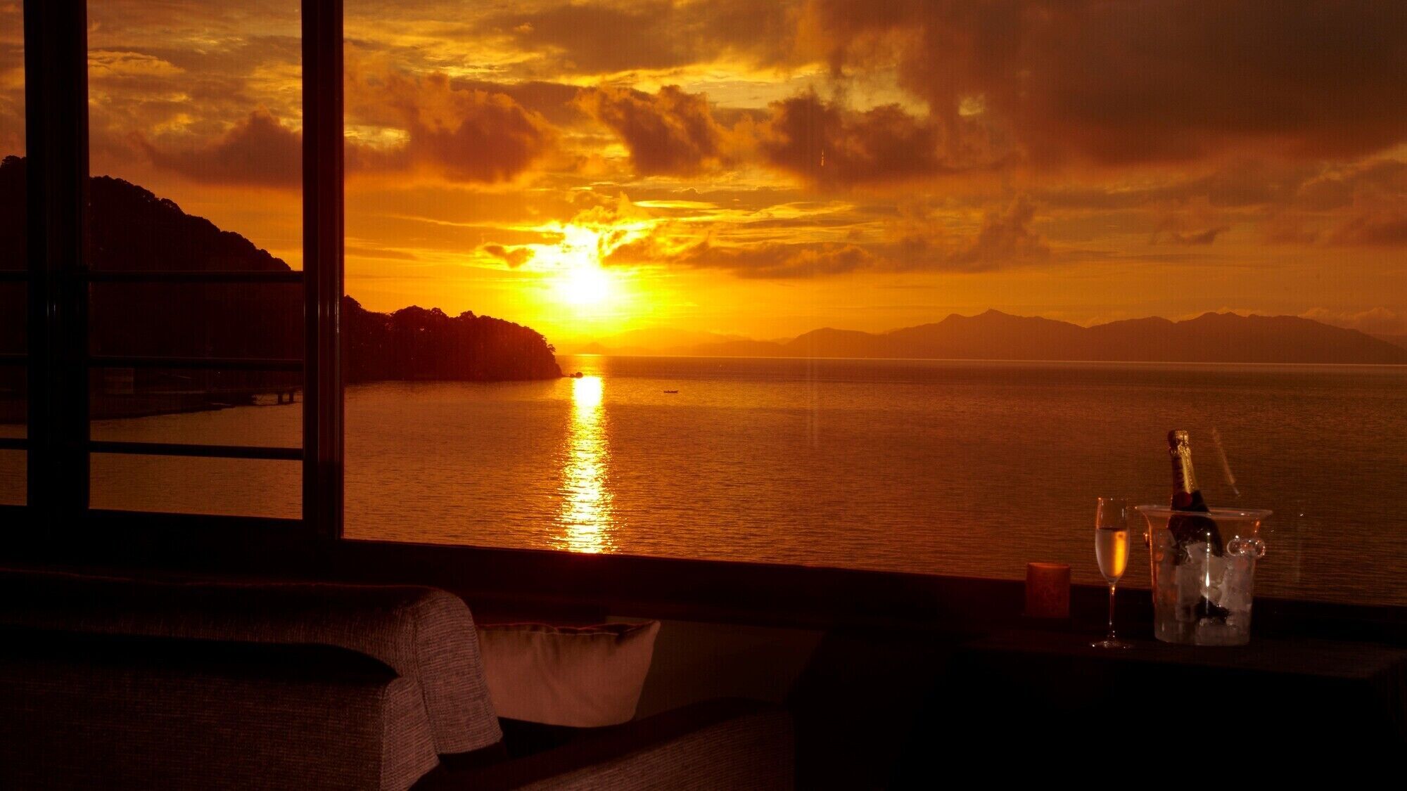 A sunset view from a room with a window, a bottle of champagne, and a candle on a table.