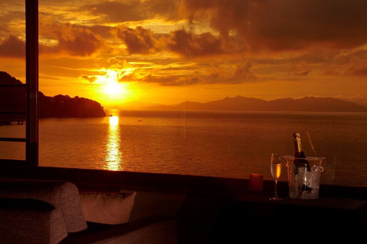 A sunset view from a room with a window, a bottle of champagne, and a candle on a table.