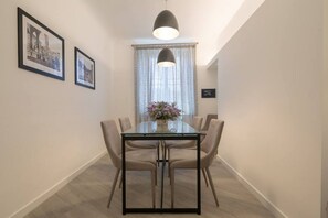 Een eethoek met een glazen tafel, zes stoelen, een hanglamp en twee ingelijste foto's aan de muur.