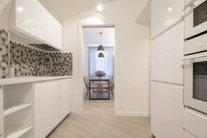Een moderne keuken met witte kastjes, een backsplash van hexagontegels en een eethoek met een tafel en stoelen.