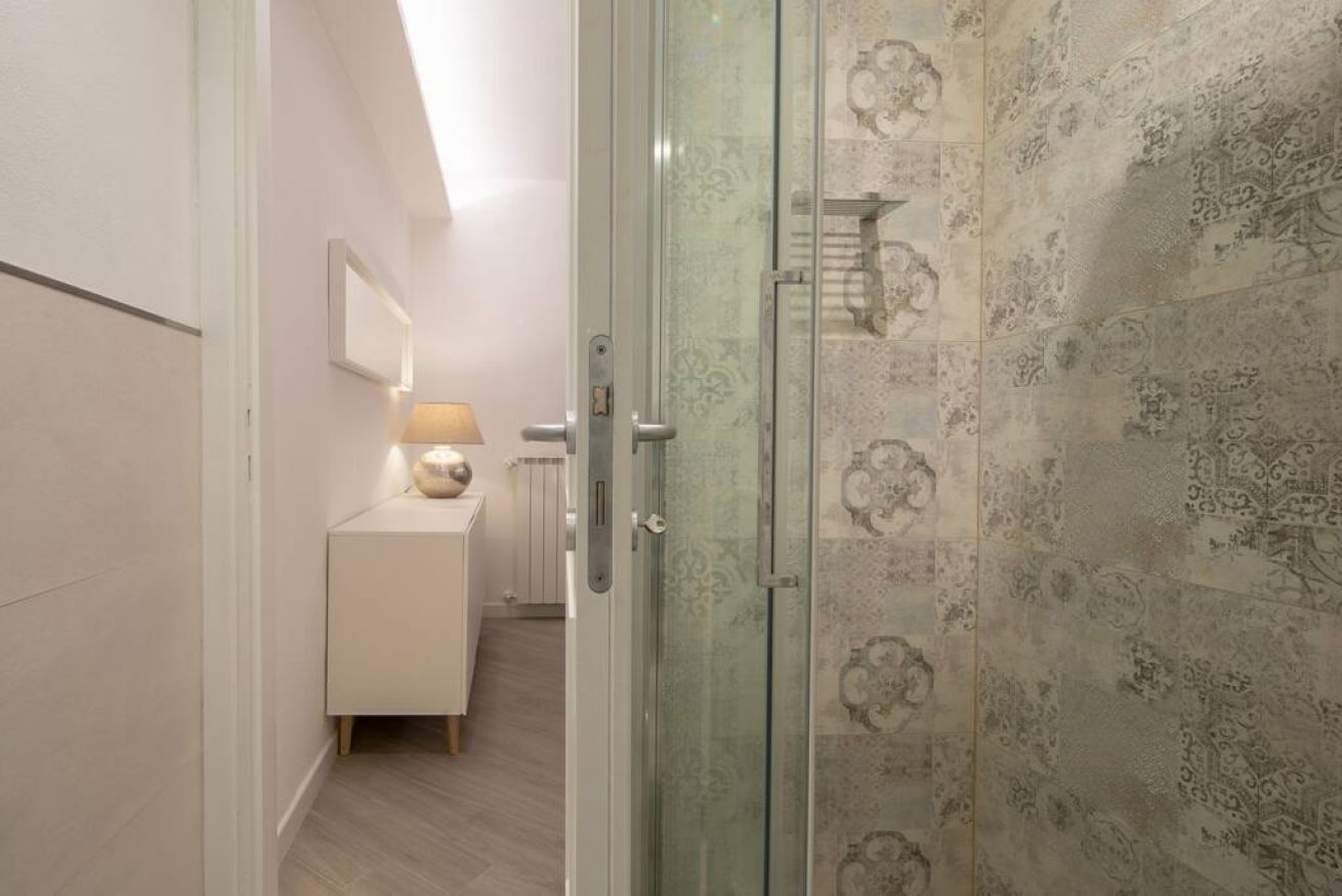 A modern bathroom with a glass shower enclosure, a white vanity with a lamp, and patterned tiles.