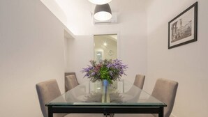 Un coin repas avec une table en verre, quatre chaises, une plante en pot et un tableau encadré au mur.