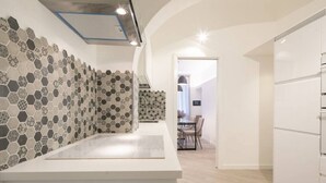 Une cuisine moderne dotée d’un plan de travail blanc, d’un crédence ornée de motifs hexagonaux et d’un coin repas avec une table et des chaises.