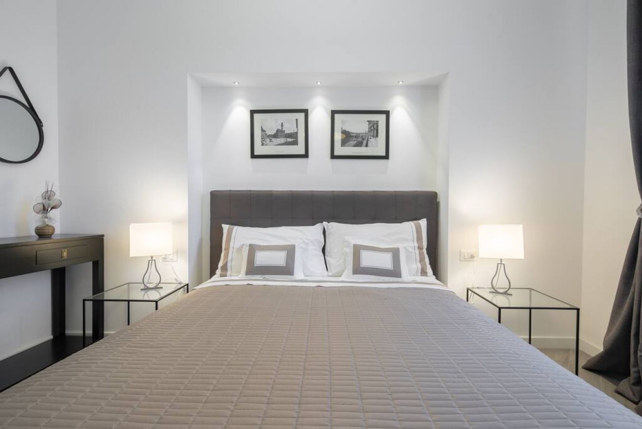Une chambre d’hôtel avec un grand lit, deux tables de chevet avec des lampes, une tête de lit sombre et deux tableaux encadrés accrochés au mur.