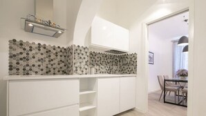 Une cuisine moderne avec des meubles blancs, un dosseret à motifs hexagonaux et un coin repas comprenant une table et des chaises.