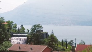 A house with a red roof, a waterfall, and a mountain in the background. - Lake view and waterfall view (Bellano)