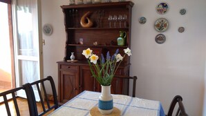 A dining table with a vase of flowers, wooden chairs, a wooden cabinet with glassware, and decorative plates on the wall. - Lake view and waterfall view (Bellano)