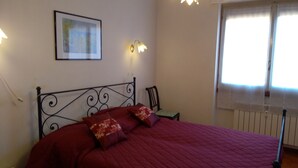 A bed with a red quilt, two pillows, a wall-mounted light, and a window with curtains. - Lake view and waterfall view (Bellano)
