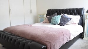 Een bed met een gestoffeerd hoofdbord, een roze sprei en meerdere kussens.