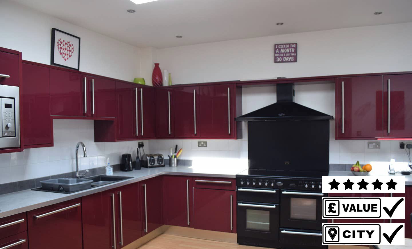 A modern kitchen with red cabinets, a black range hood, and stainless steel appliances.