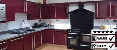 A modern kitchen with red cabinets, a black range hood, and stainless steel appliances.